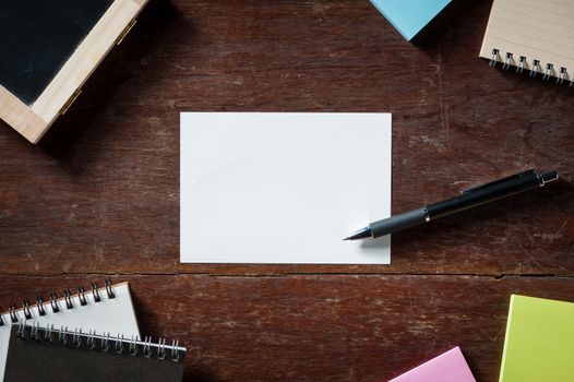 Blank paper with area for text or message, pen, notebook, and sticky paper on wood table with low key scene