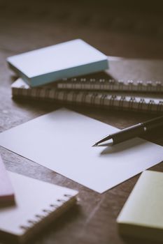 Blank paper on wood table with notebooks on wood table with low key scene and vintage filter effect