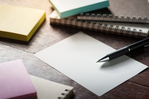 Blank paper on wood table with notebooks on wood table with low key scene