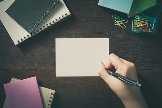 Woman right hand writing on notepad with blank area for text or message on wood table with low key scene and vintage filter effect