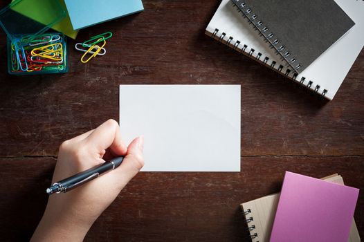 Woman left hand writing on notepad with blank area for text or message on wood table with low key scene
