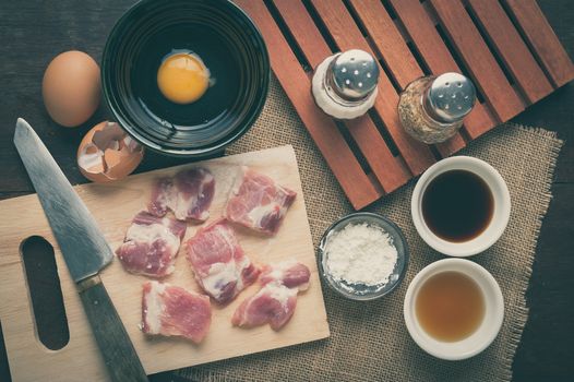 Preparation for cooking in home kitchen. Soft pork ribs on chopping board, eggs, and ingredients on wood table with vintage filter effect