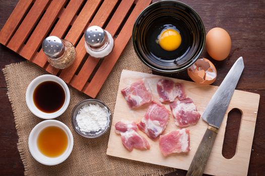 Preparation for cooking in home kitchen. Soft pork ribs on chopping board, eggs, and ingredients on wood table.