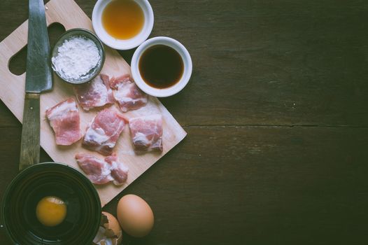 Preparation for cooking in home kitchen. Soft pork ribs on chopping board, eggs, and ingredients on wood table with vintage filter effect