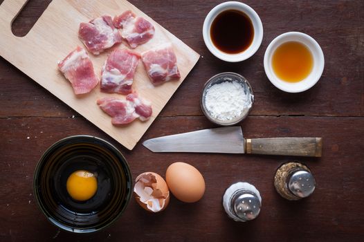 Preparation for cooking in home kitchen. Soft pork ribs on chopping board, eggs, and ingredients on wood table.