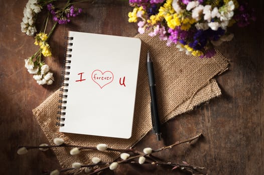 "I love you forever" is written on notebook on wood table with low key scene
