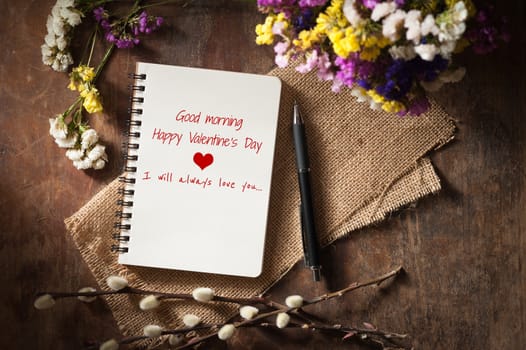 "Good morning Happy valentine's day I will always love you" is written on opened notebook on wood table with low key scene
