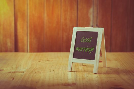 "Good morning" is written on small A-frame black board with blank area for text or message on wood table with vintage filter effect
