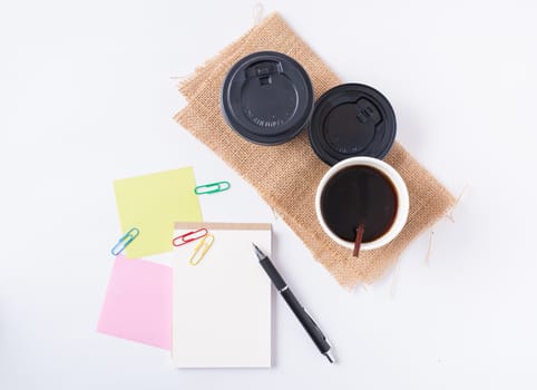 Small notepad with blank space for text or message, sticky paper, pen and take away coffee cup on office table.