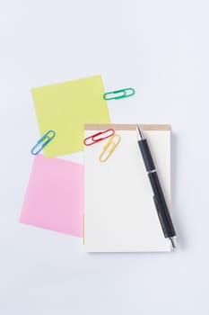 Small notepad with blank space for text or message, sticky paper, pen and paper clips on office table.