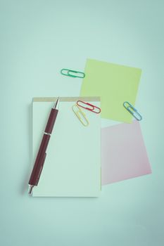 Small notepad with blank space for text or message, sticky paper, pen and paper clips on office table. with vintage filter effect