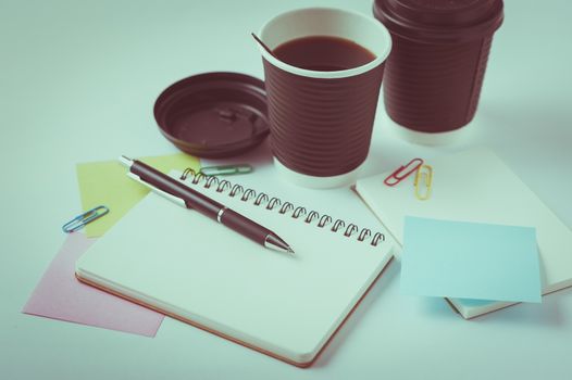 Opened notebook, pen, sticky paper, and take away coffee cup on office table with vintage filter effect