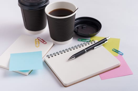 Opened notebook, pen, sticky paper, and take away coffee cup on office table