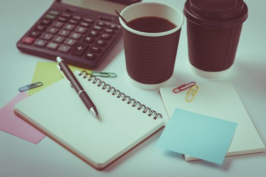 Opened notebook, pen, sticky paper, and take away coffee cup on office table with vintage filter effect