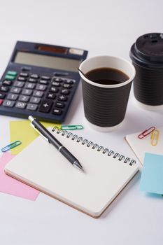Opened notebook, pen, sticky paper, and take away coffee cup on office table
