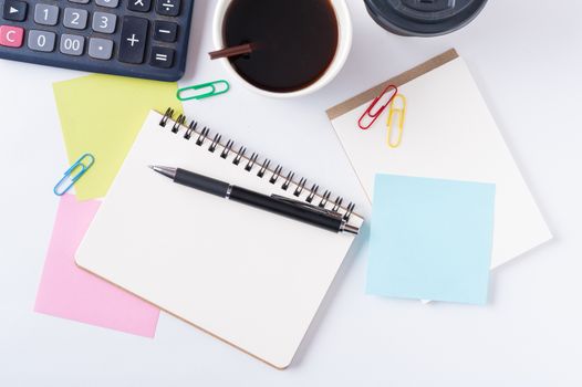 Opened notebook with blank space for text or message, sticky paper, calculator, and take away coffee cup on office table
