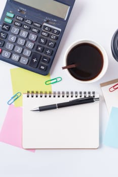 Opened notebook with blank space for text or message, sticky paper, calculator, and take away coffee cup on office table