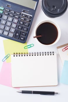 Opened notebook with blank space for text or message, sticky paper, calculator, and take away coffee cup on office table