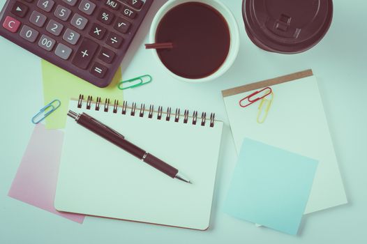 Opened notebook with blank space for text or message, sticky paper, calculator, and take away coffee cup on office table