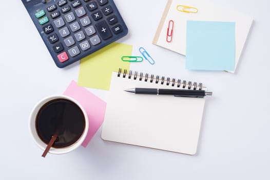 Opened notebook with blank space for text or message, sticky paper, calculator, and take away coffee cup on office table