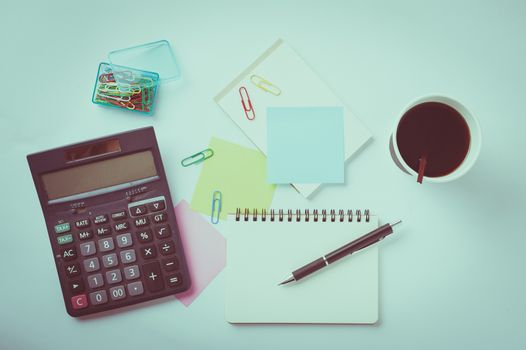 Opened notebook with blank space for text or message, sticky paper, calculator, and take away coffee cup on office table with vintage filter effect