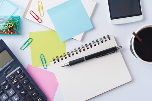 Opened notebook with blank space for text or message, sticky paper, calculator, and take away coffee cup on office table