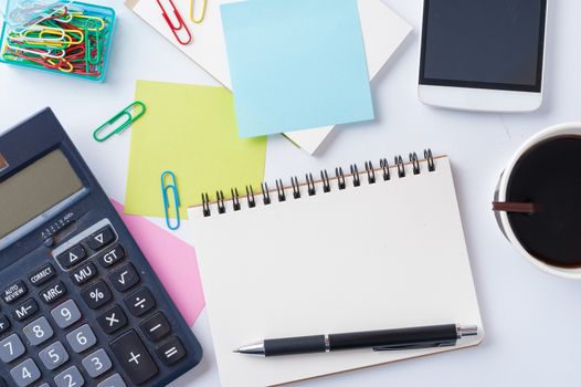 Opened notebook with blank space for text or message, sticky paper, calculator, smart phone, and take away coffee cup on office table