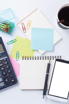 Opened notebook with blank space for text or message, sticky paper, calculator, smart phone, and take away coffee cup on office table
