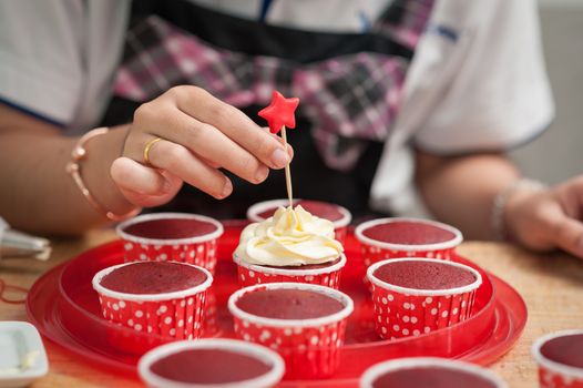 The action of making red velvet cupcakes. Woman hand stab down star shape fondant on cupcake
