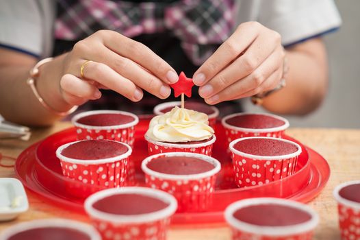 The action of making red velvet cupcakes. Woman hand stab down star shape fondant on cupcake