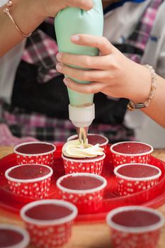 The action of making red velvet cupcakes. Woman hand piping cream cheese on cupcake.