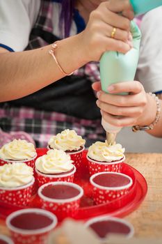 The action of making red velvet cupcakes. Woman hand piping cream cheese on cupcake.