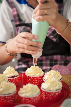 The action of making red velvet cupcakes. Woman hand piping cream cheese on cupcake.