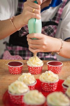 The action of making red velvet cupcakes. Woman hand piping cream cheese on cupcake.