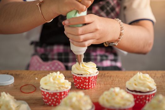The action of making red velvet cupcakes. Woman hand piping cream cheese on cupcake.