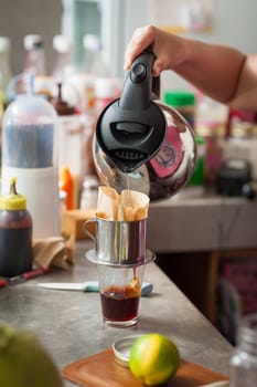 The process of making Thai lemon tea. Woman right hand pouring hot water into dripper above tea glass