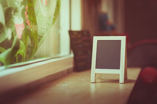 Small A-frame black board with blank area for text or message on wood bar in cafe wih vintage filter effect
