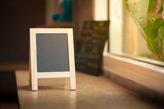 Small A-frame black board with blank area for text or message on wood bar in cafe wih low key scene