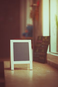 Small A-frame black board with blank area for text or message on wood bar in cafe wih vintage filter effect