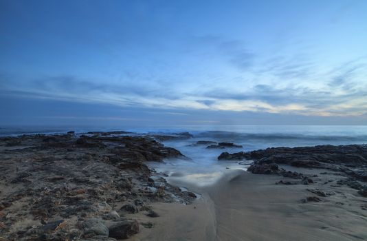 Long exposure of sunset over rocks, giving a mist like effect over ocean in Laguna Beach, California, United States