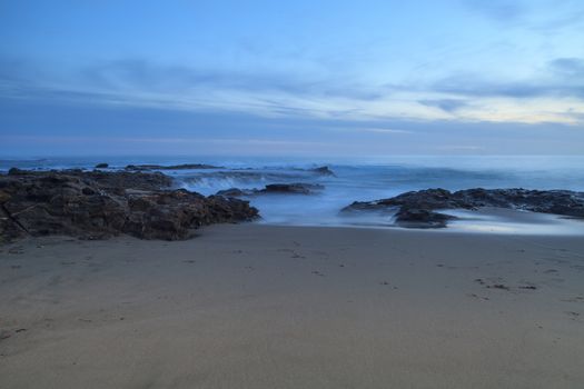 Long exposure of sunset over rocks, giving a mist like effect over ocean in Laguna Beach, California, United States