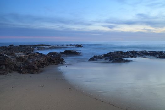 Long exposure of sunset over rocks, giving a mist like effect over ocean in Laguna Beach, California, United States