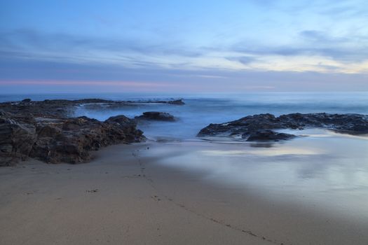 Long exposure of sunset over rocks, giving a mist like effect over ocean in Laguna Beach, California, United States