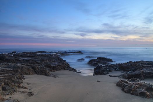 Long exposure of sunset over rocks, giving a mist like effect over ocean in Laguna Beach, California, United States