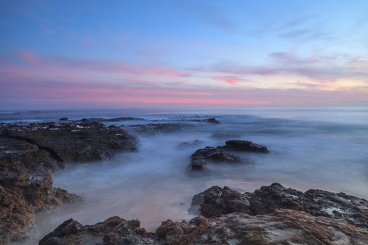 Long exposure of sunset over rocks, giving a mist like effect over ocean in Laguna Beach, California, United States