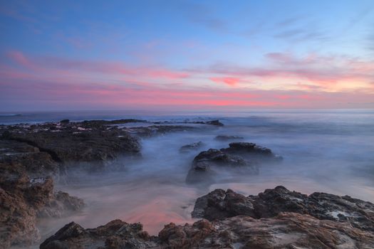 Long exposure of sunset over rocks, giving a mist like effect over ocean in Laguna Beach, California, United States