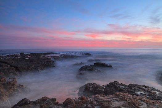 Long exposure of sunset over rocks, giving a mist like effect over ocean in Laguna Beach, California, United States