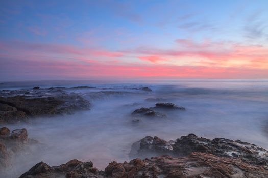 Long exposure of sunset over rocks, giving a mist like effect over ocean in Laguna Beach, California, United States