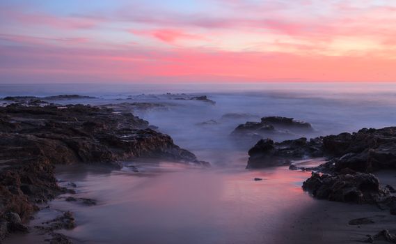 Long exposure of sunset over rocks, giving a mist like effect over ocean in Laguna Beach, California, United States