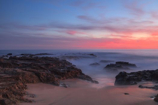 Long exposure of sunset over rocks, giving a mist like effect over ocean in Laguna Beach, California, United States